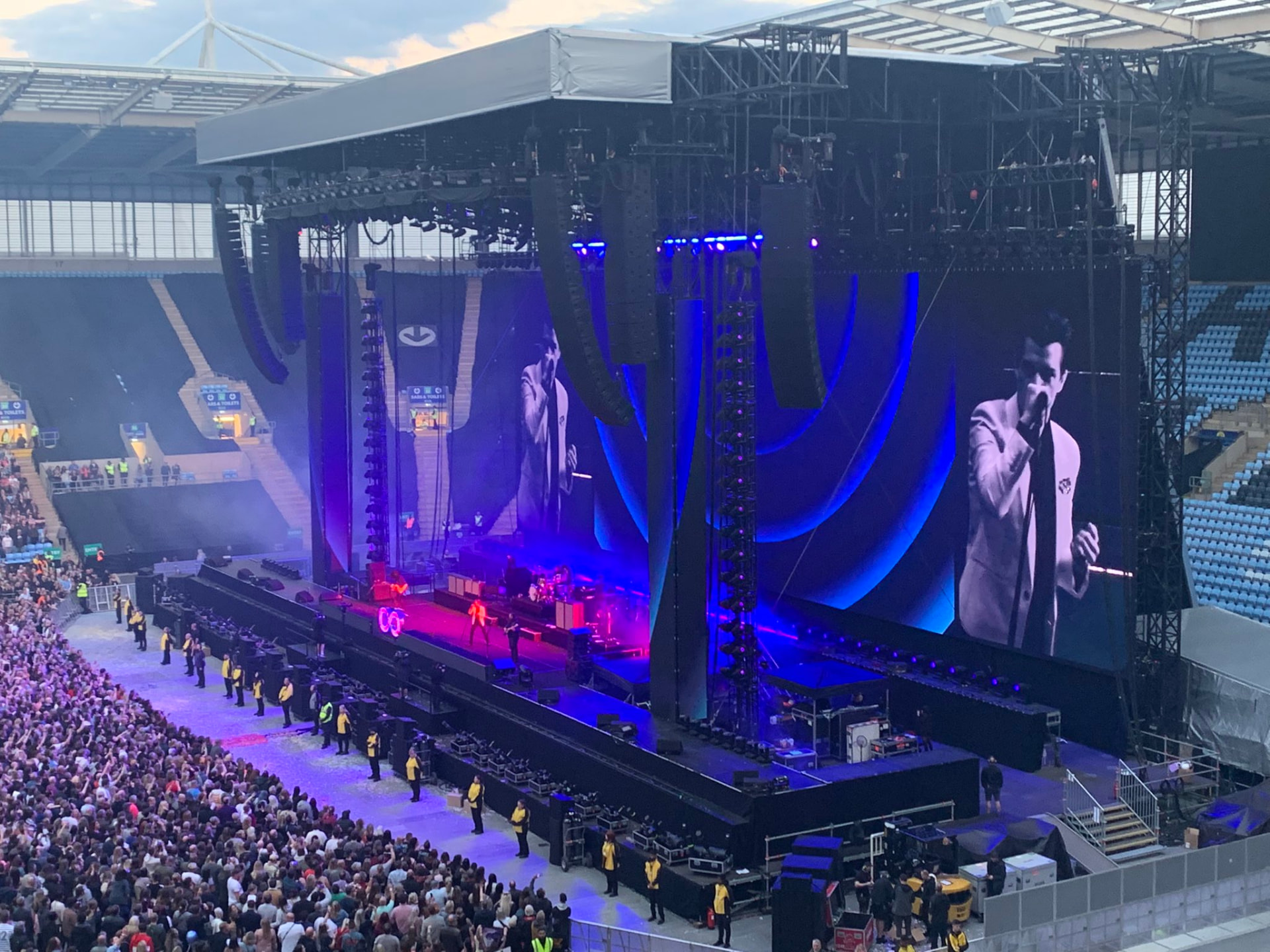 Live stadium concert with security personnel positioned along the front of the audience