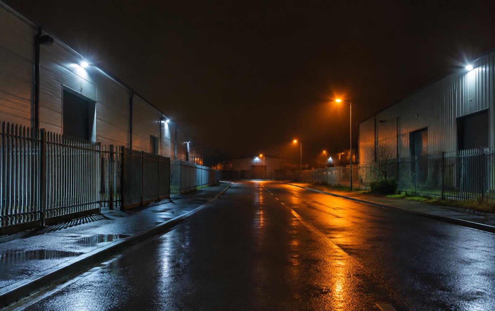 Empty UK industrial estate road at night lit by floodlights and street lamps