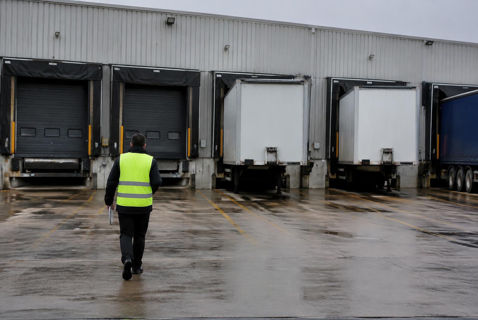Security officer walking past warehouse loading bays with trailers docked